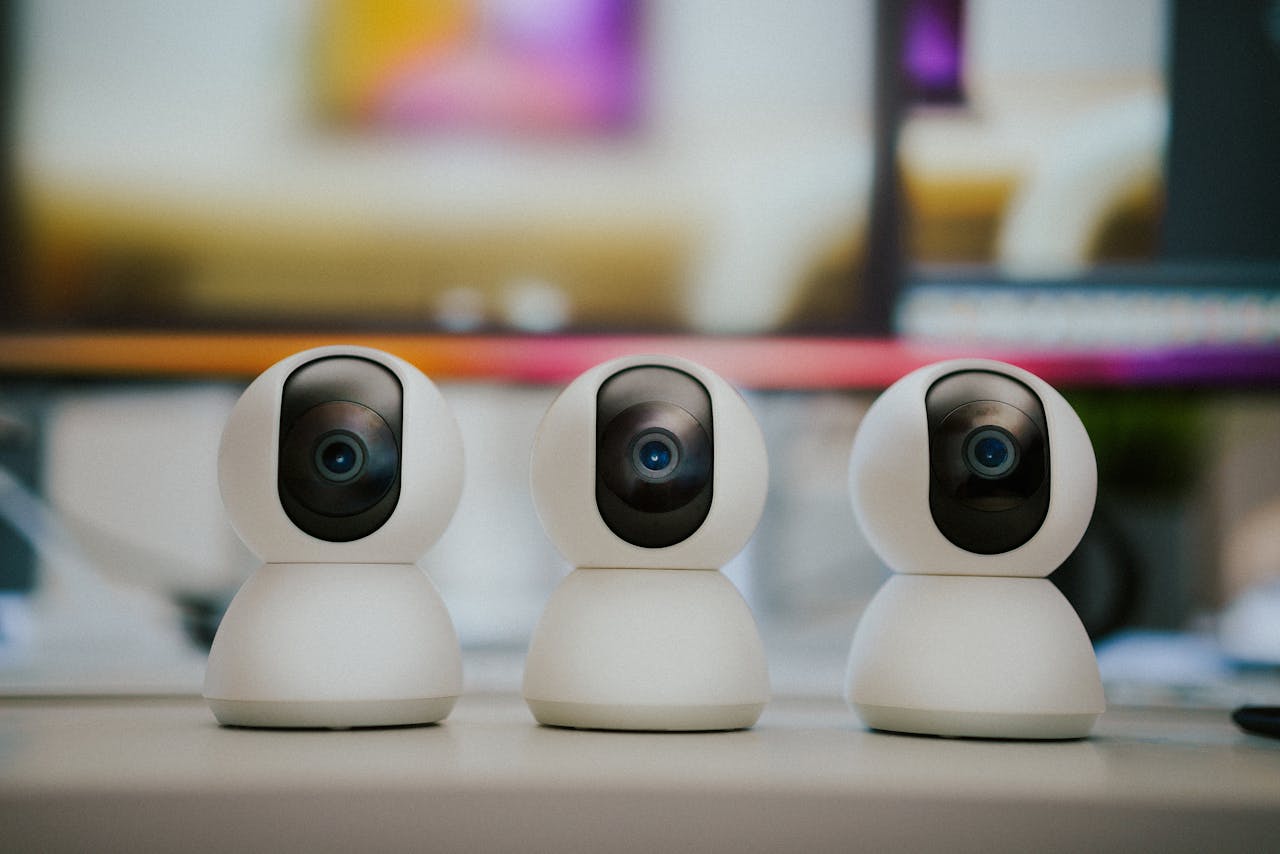 team-01 Three modern smart home security cameras placed on a table indoors with a blurry background.